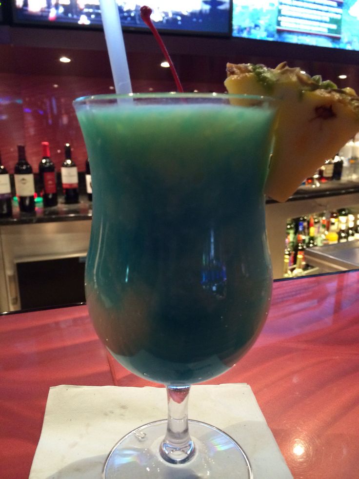 a blue drink sitting on top of a table in front of a tv screen at a bar