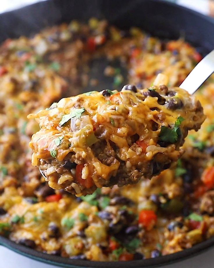 a spoonful of mexican rice and beans is being lifted from a skillet with a spatula