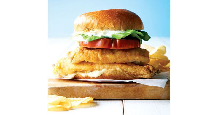 a chicken sandwich with lettuce, tomato and mayonnaise on a cutting board