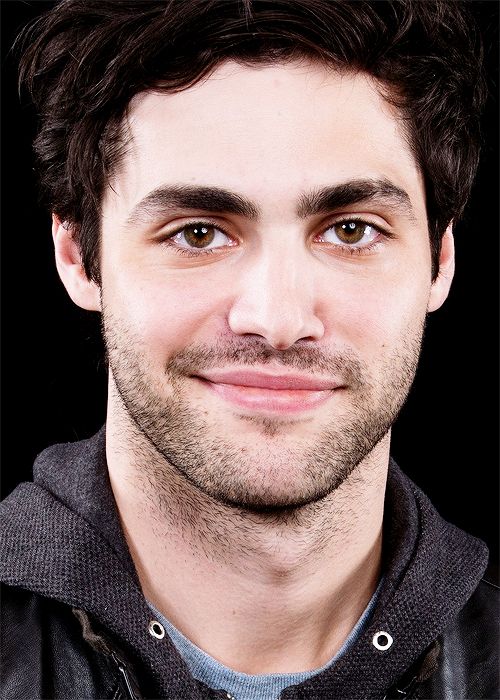 a close up of a person wearing a jacket and smiling at the camera with a black background