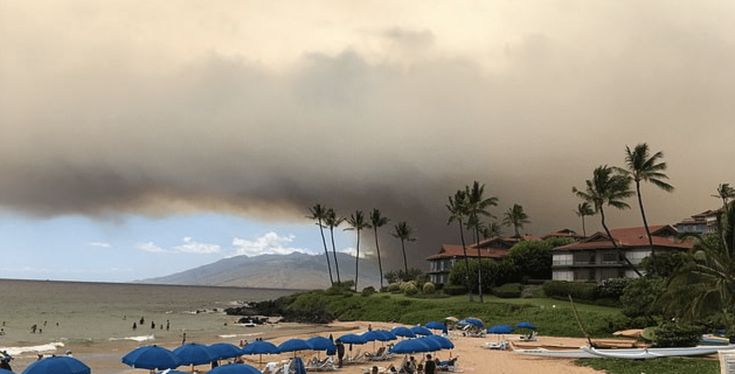 a beach with umbrellas and people on it under a large cloud in the sky