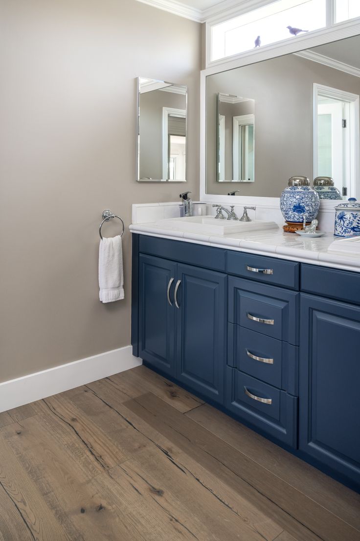 a blue and white bathroom with wood flooring, two sinks and large mirrors on the wall