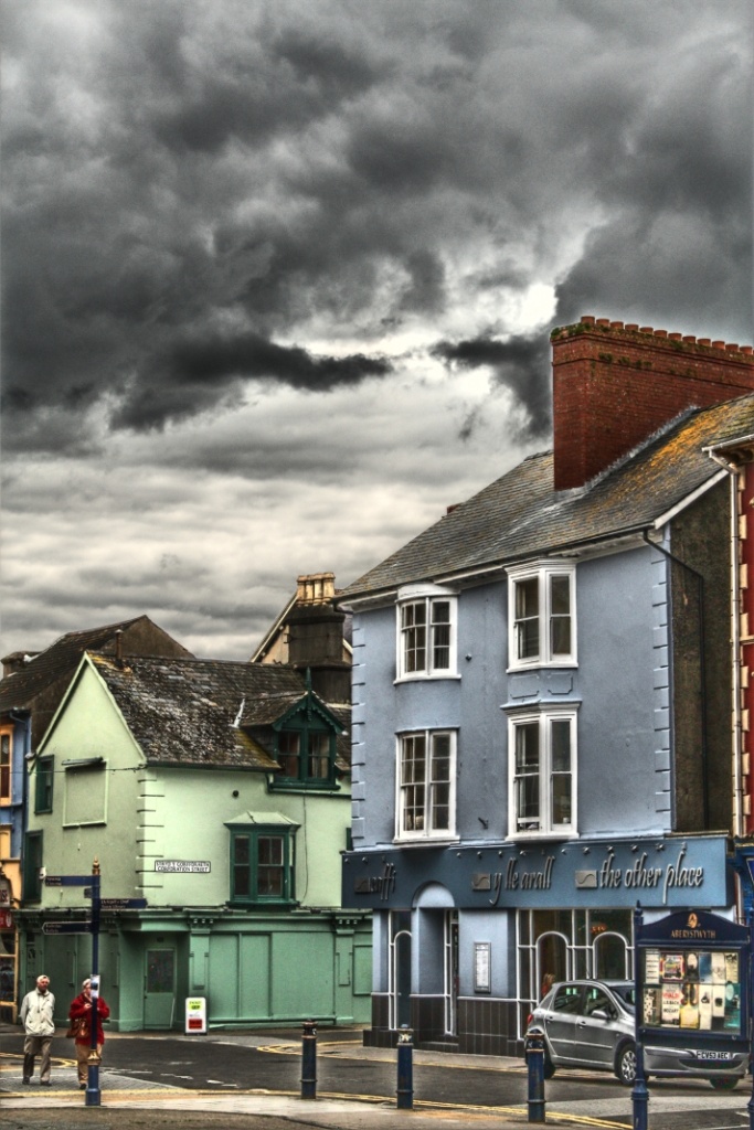 some people are walking down the street in front of some buildings and storm clouds above them