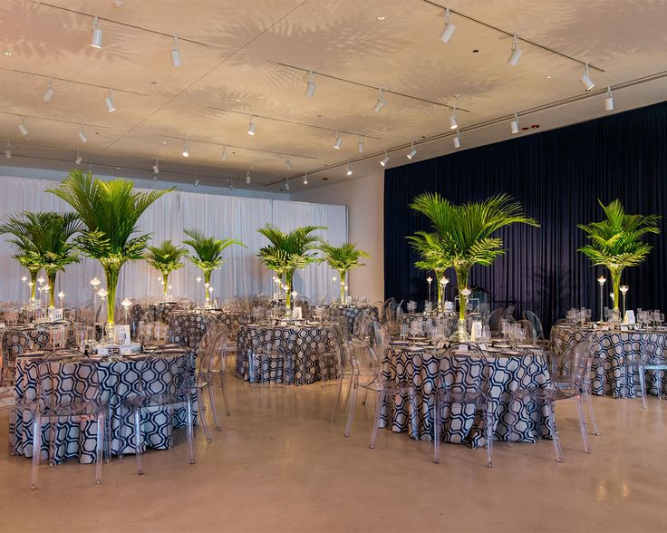 a banquet hall with tables and chairs covered in blue cloths, decorated with palm trees