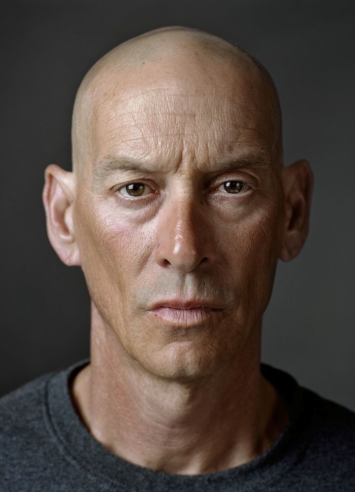 a bald man in a gray shirt looking at the camera with an intense look on his face