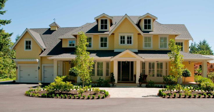 a large yellow house with lots of trees and bushes around it's front entrance