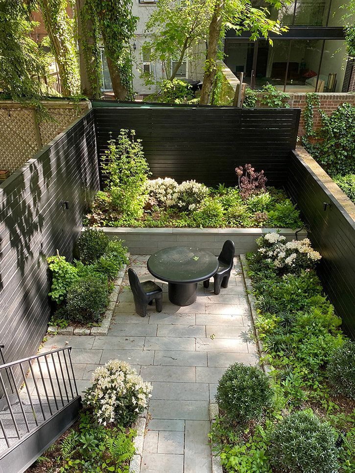 an outdoor dining area with tables and chairs surrounded by greenery in the back yard