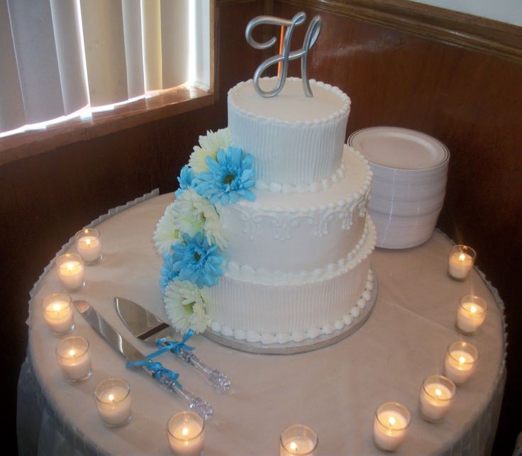 a three tiered white cake with blue flowers and candles around it on a table