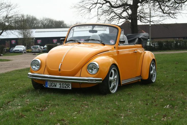 an orange vw bug is parked in the grass