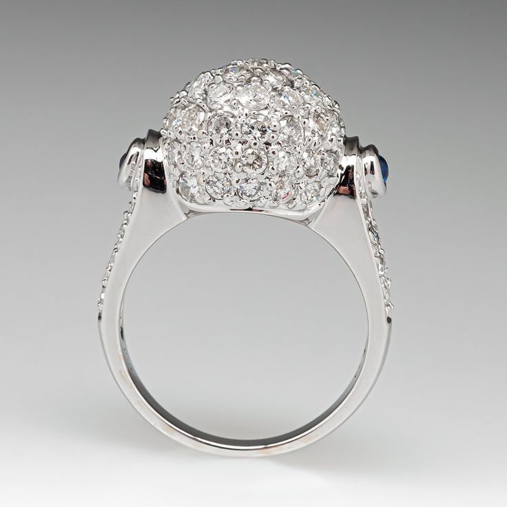 This awesome ring is centered with a domed setting accented with forty-seven (47), bead set, round brilliant cut diamonds. The shoulders of the ring are each accented with one (1), bezel set, round cabochon cut natural sapphire and eight (8), bead set, round brilliant cut diamonds. The ring measures 13.5mm at the top, rises 10.1mm above the finger, tapering to 2.5mm wide and 1.1mm thick at the base of the shank. This ring is currently a size 6.75. Luxury Oval Cluster Ring With Single Cut Diamonds, Dazzling Sapphire Ring With Brilliant Cut Diamond, Oval Sapphire Ring With Pave Setting In Platinum, Classic Multi-stone Diamond White Diamond Ring, Luxury Round Ring With Diamond Accents, Diamond White Cluster Ring In Fine Jewelry Style, Luxury Round Rings With Diamond Accents, Classic Multi-stone Platinum Diamond Ring, Luxury Cluster Ring With Pave Setting For Formal Occasions