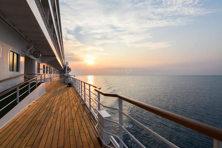 the deck of a cruise ship as the sun sets over the ocean in the distance