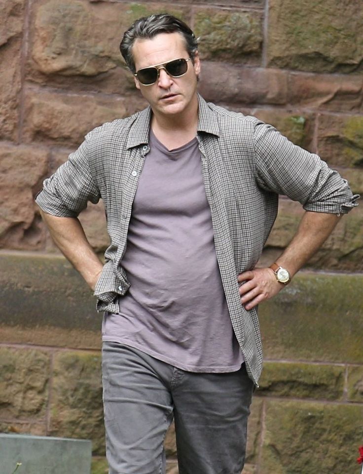 a man with his hands on his hips standing in front of a brick wall wearing sunglasses