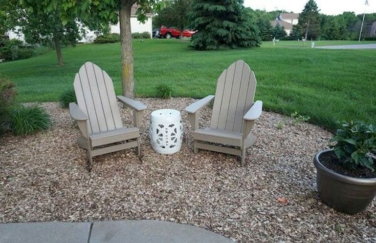 two adiron chairs sitting in the middle of a gravel area next to a potted plant