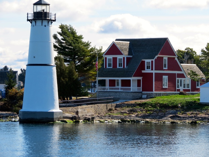 a red and white house next to a body of water with a lighthouse in the background