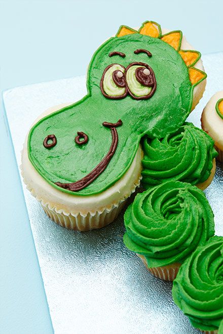 some cupcakes with green frosting and a dinosaur face on top are sitting next to each other