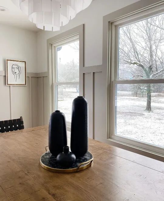 two black vases sitting on top of a wooden table in front of a window