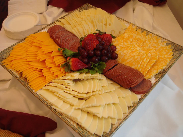 a platter filled with cheese, fruit and sausages on top of a table