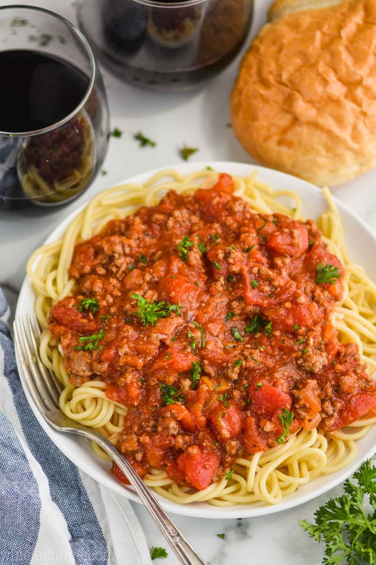 a white plate topped with spaghetti and meat sauce next to bread on a marble table