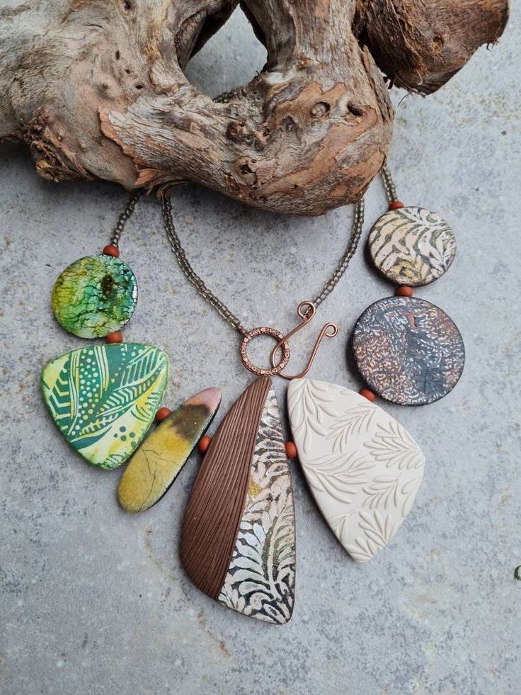 a necklace with different colored stones hanging from it's chain next to a piece of driftwood