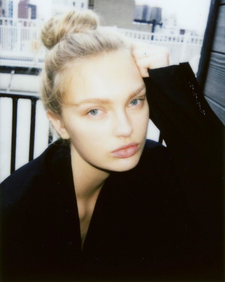 a woman with blonde hair wearing a black shirt and holding her hand on her head