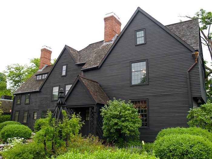 an old black house surrounded by greenery and trees