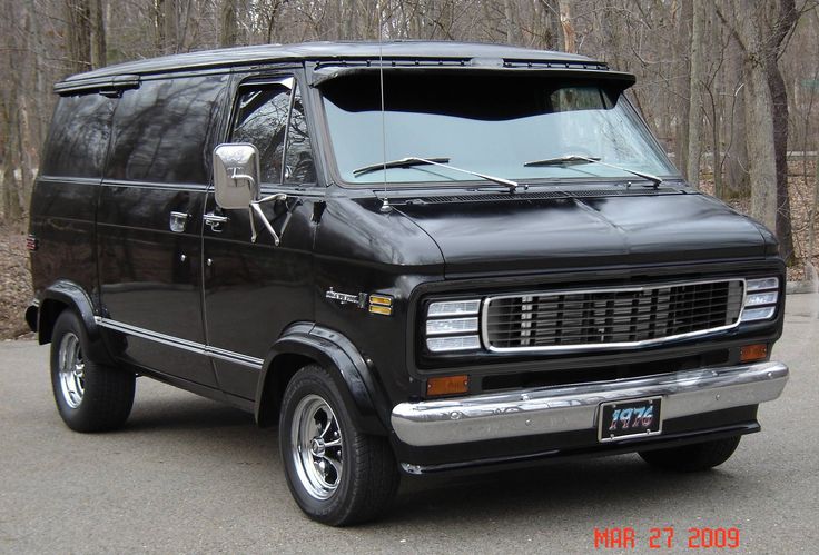 an old black van parked in front of some trees