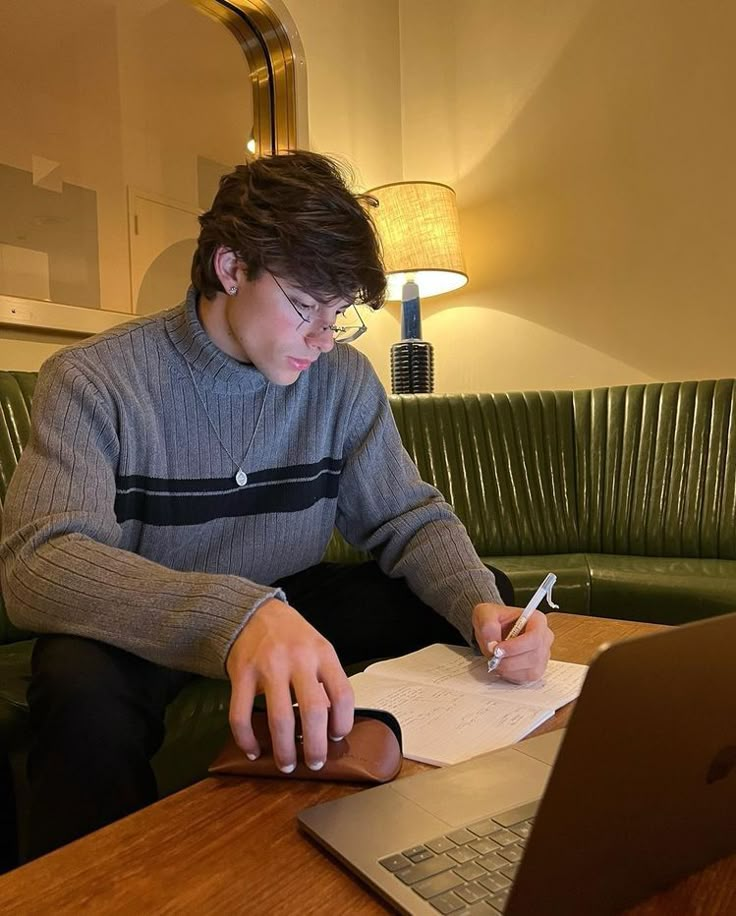 a man sitting at a table with a laptop and pen in his hand while writing on paper