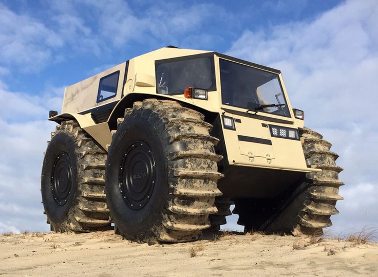 an off - road vehicle with large tires is driving through the sand on a cloudy day