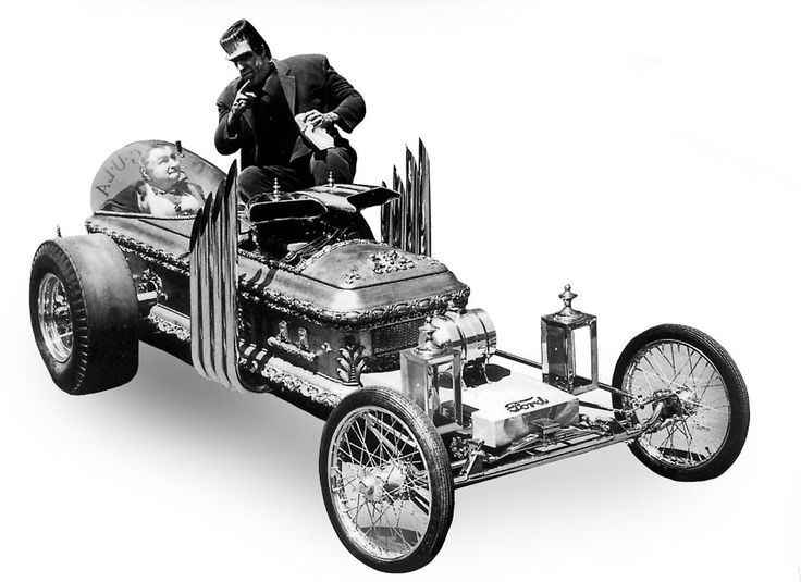 an old fashioned car with a man sitting on the engine and looking at his cell phone