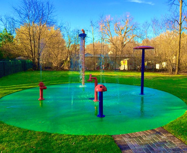 a colorful fountain in the middle of a green park with trees and blue sky behind it