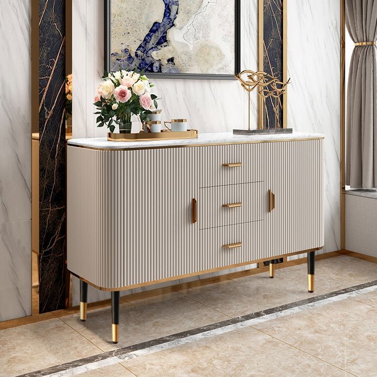 a white and gold sideboard with flowers on it in front of a large painting