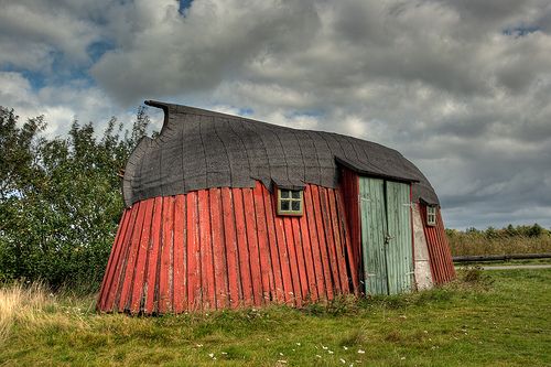 an old red barn with a thatched roof in the middle of a grassy field