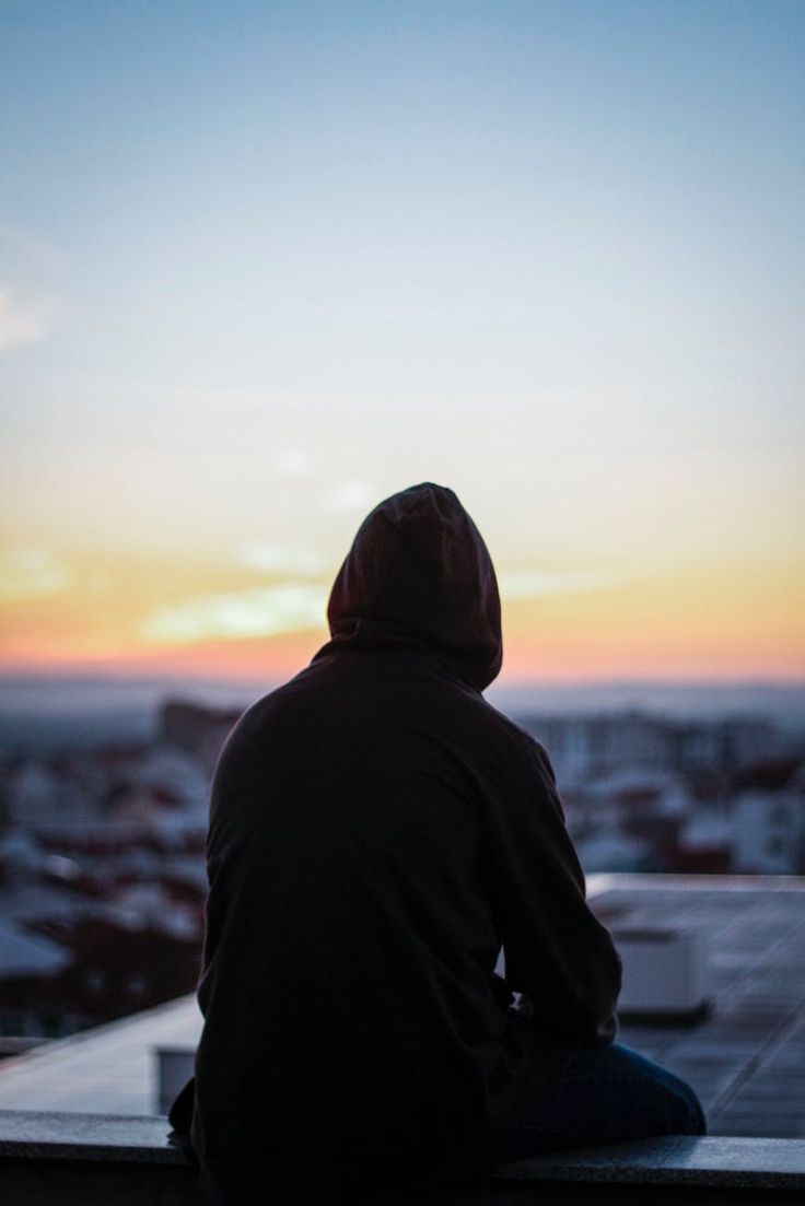 a man sitting on top of a roof looking at the sunset