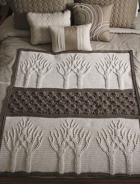 a crocheted blanket on top of a bed next to pillows