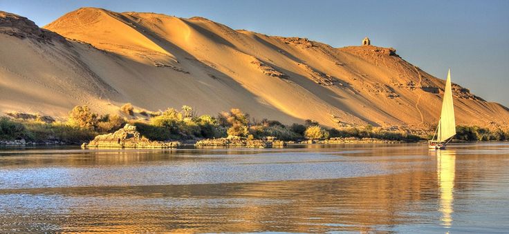 a sailboat is on the water in front of sand dunes