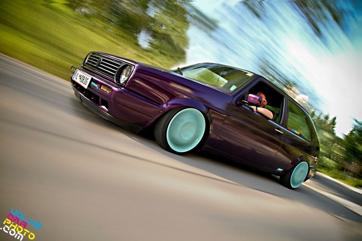 a purple car driving down the road with trees in the backgrouund and blue sky