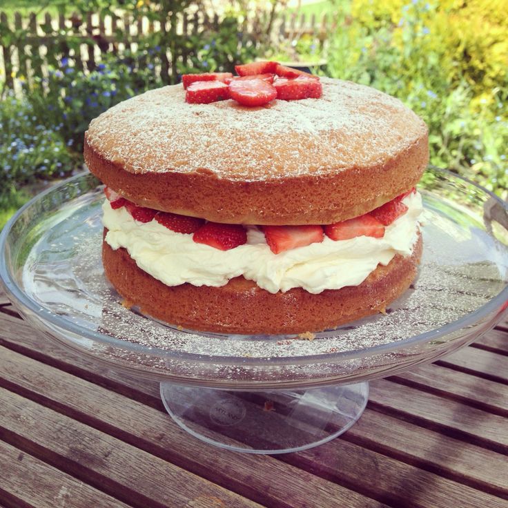 a cake with strawberries on top is sitting on a glass platter in the garden