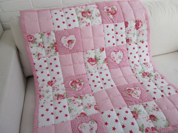 a white couch with a pink quilt on it's back and two hearts in the center