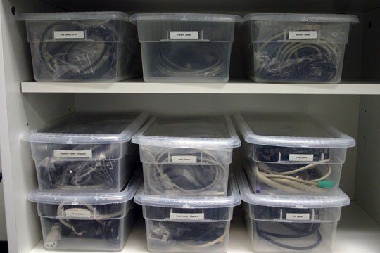 several plastic containers are stacked on top of each other in front of a shelf with wires and cords