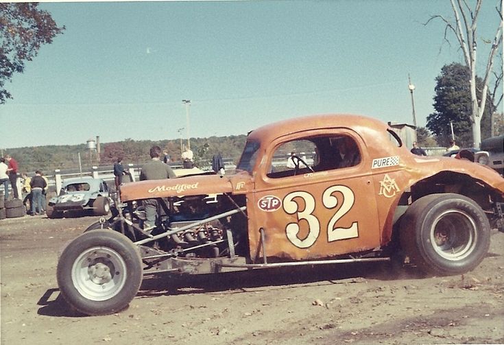 an orange race car with number 32 on it's side and people standing around in the background