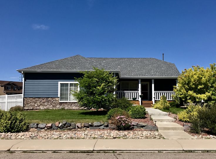 a blue house sitting on top of a lush green field next to a sidewalk and trees