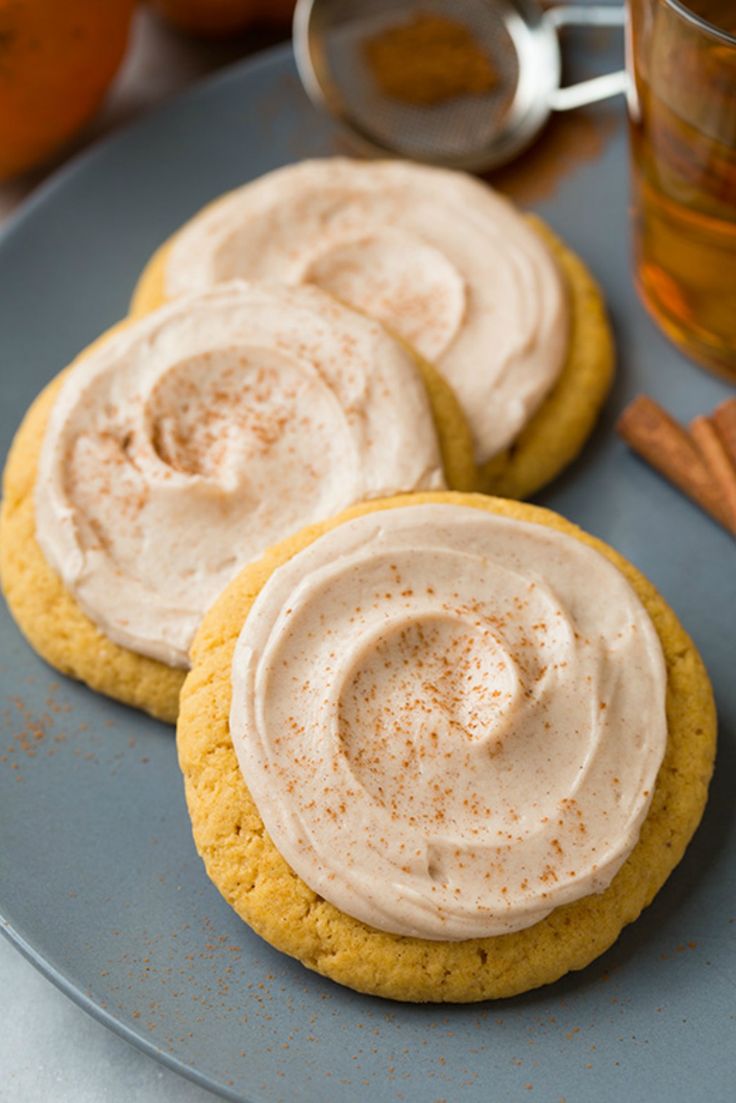 three cookies with frosting and cinnamon on a plate next to a glass of tea