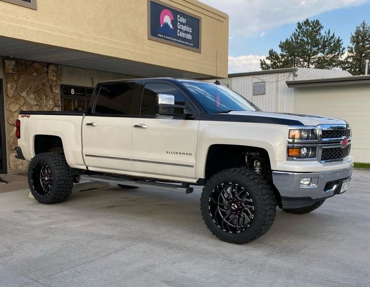 a white truck is parked in front of a building with black tires and rims