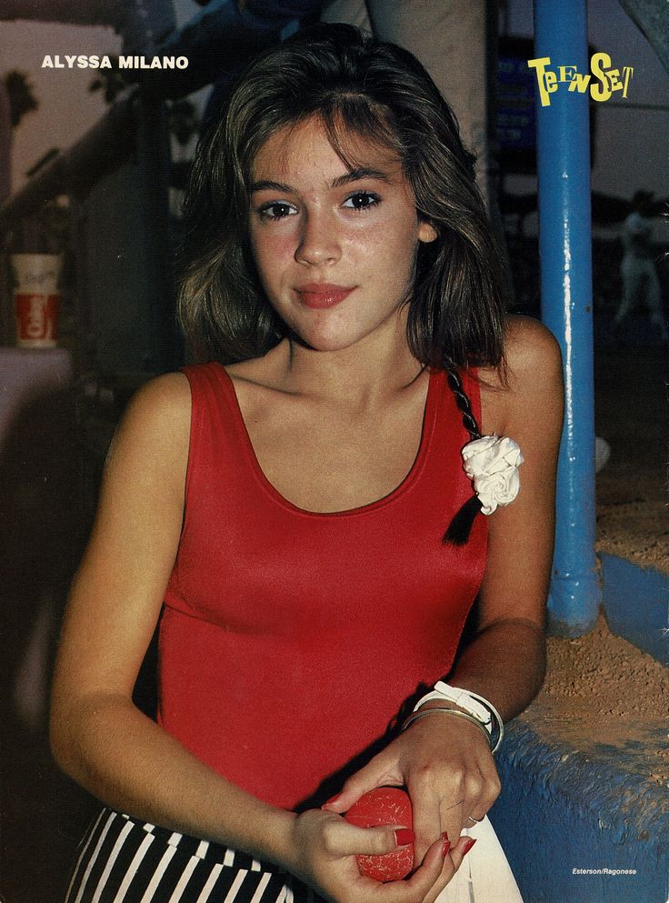 a young woman in a red tank top holding a white bag and posing for the camera