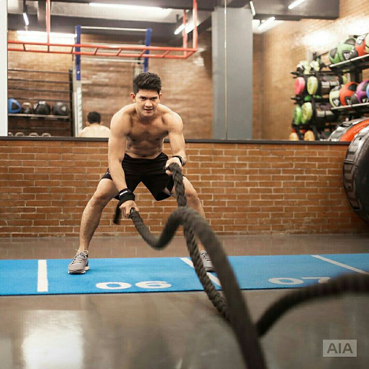 a shirtless man is doing exercises with a rope in a gym while another man watches