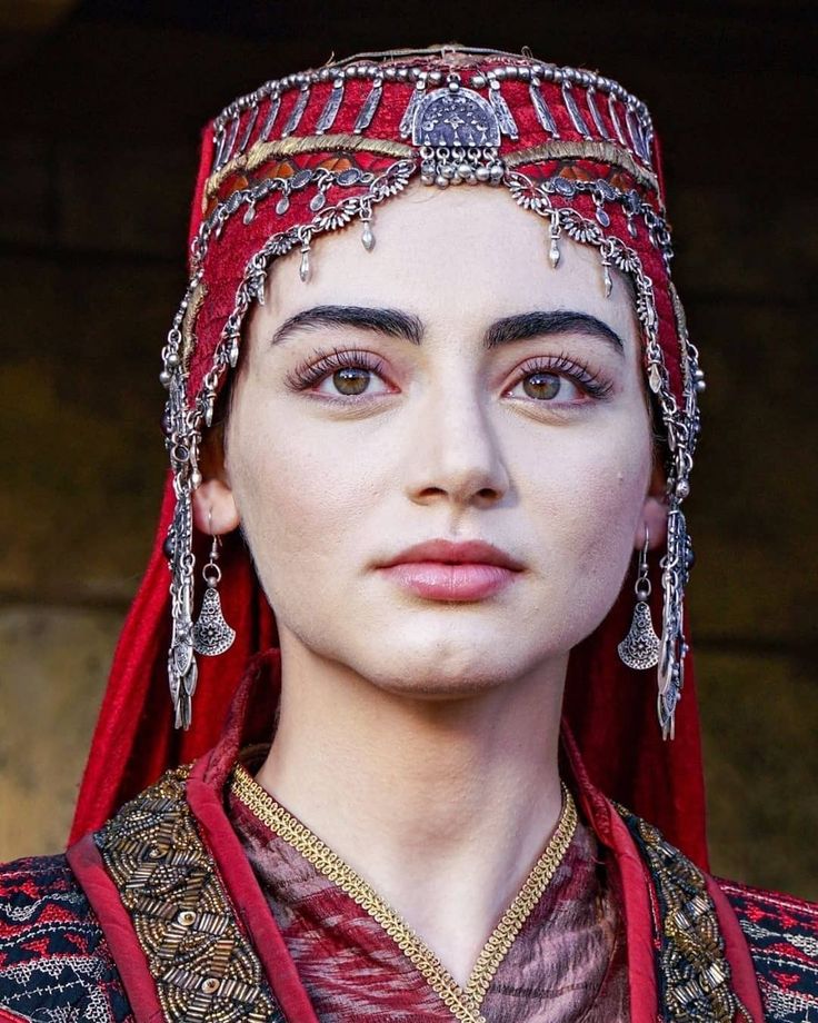 a close up of a person wearing a red dress and headpiece with jewelry on it