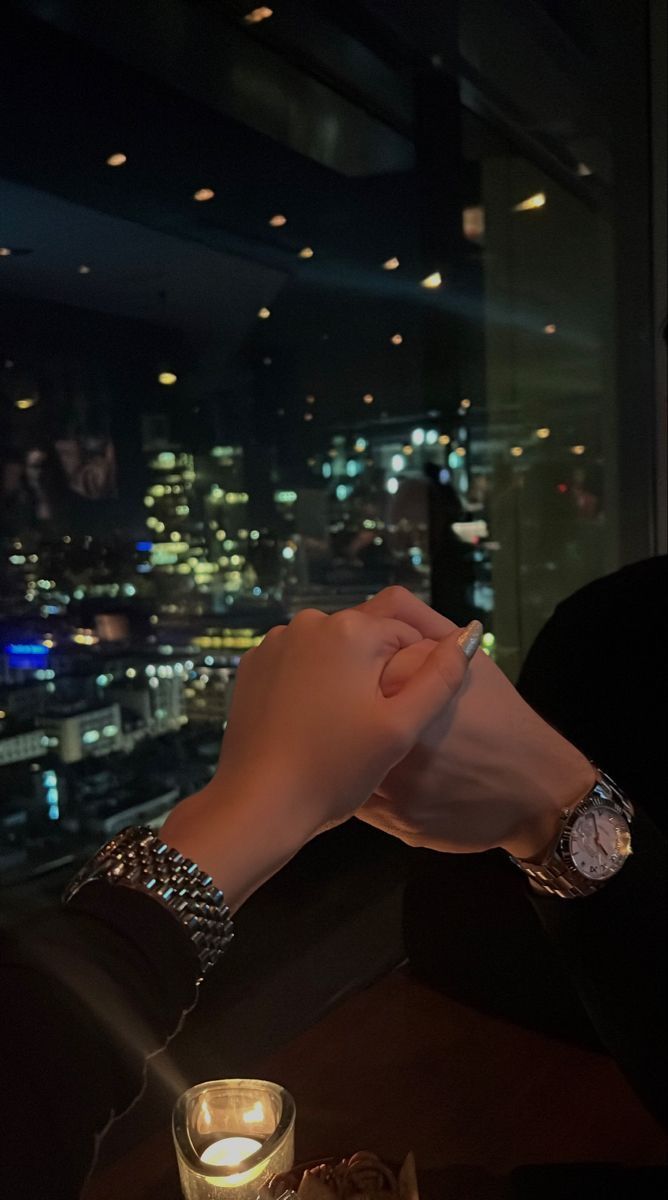 two people holding hands at a table with candles in front of the cityscape