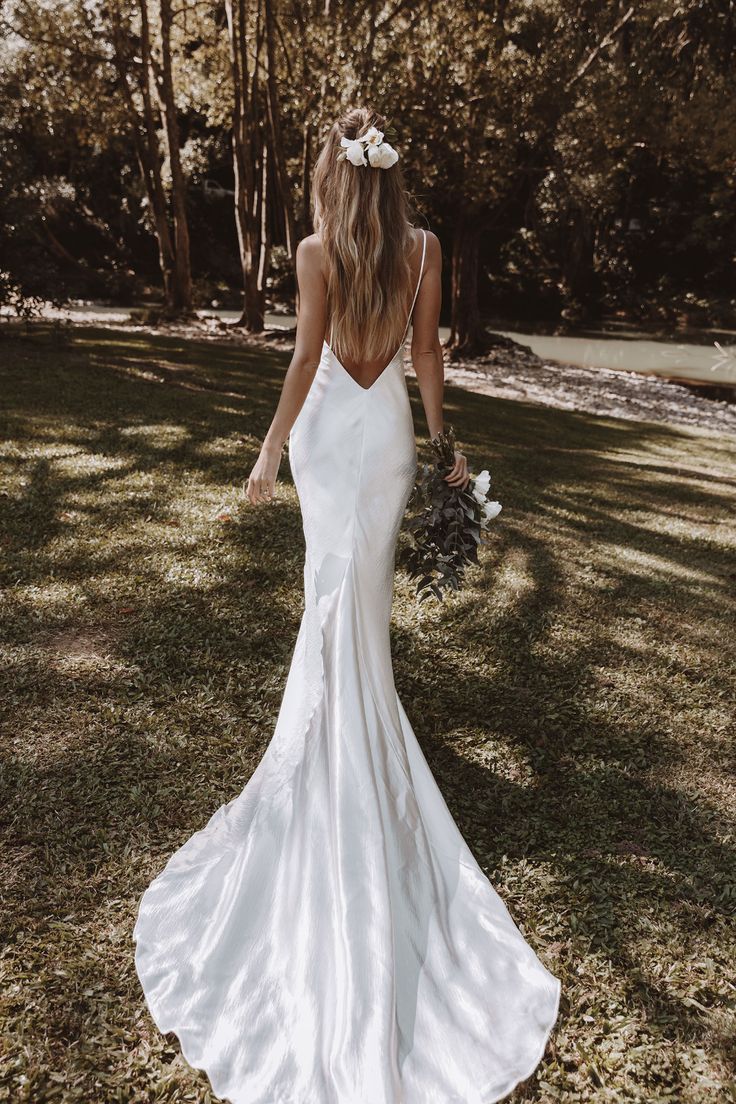 a woman in a wedding dress walking through the grass with her back to the camera