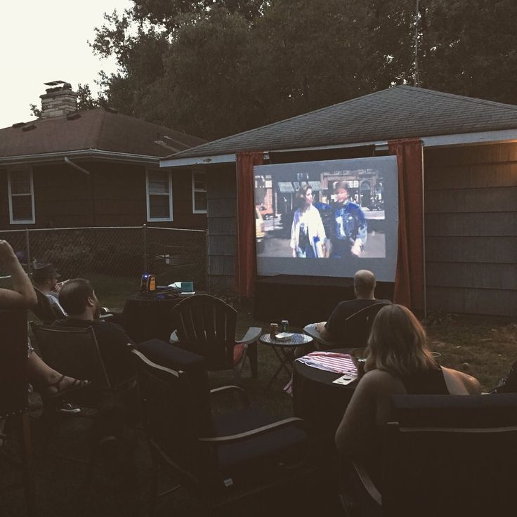 people sitting in lawn chairs watching a movie on the big screen outside at night time