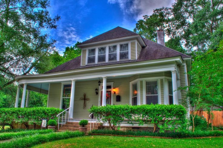 a house that is in the middle of some trees and grass with bushes around it